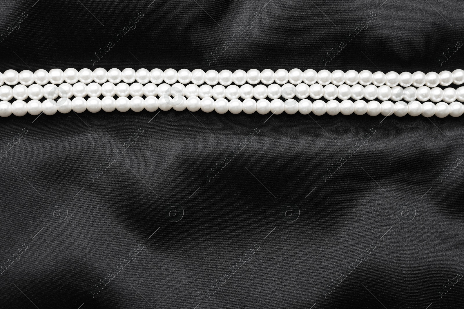 Photo of Beautiful pearl necklace on black cloth, top view. Space for text