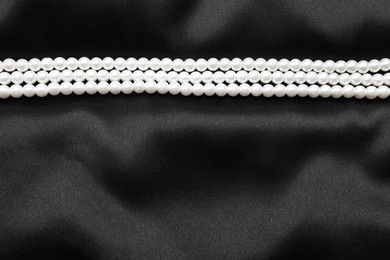 Photo of Beautiful pearl necklace on black cloth, top view. Space for text