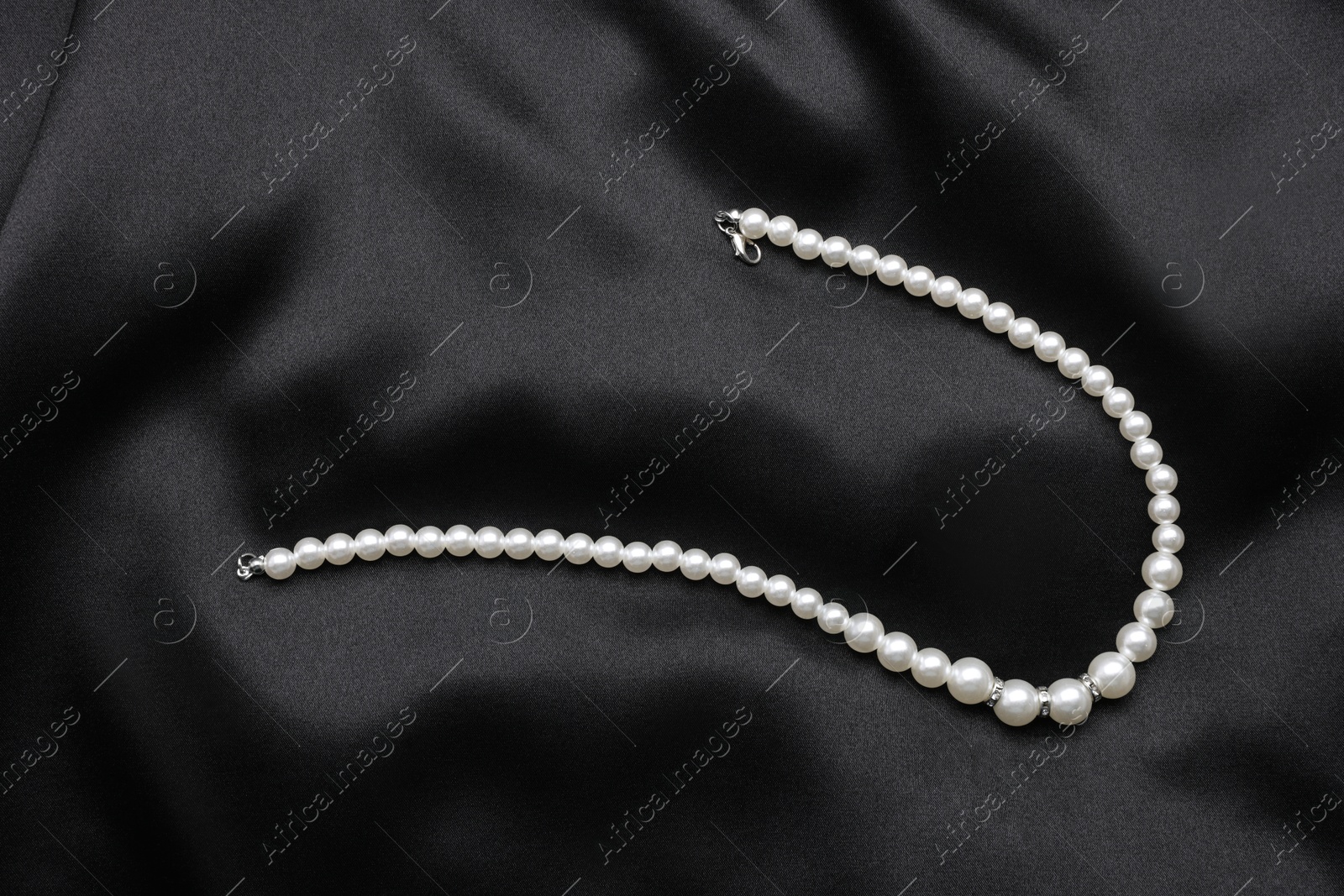 Photo of Beautiful pearl necklace on black cloth, top view