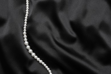 Photo of Beautiful pearl necklace on black cloth, top view. Space for text