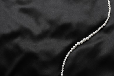 Photo of Beautiful pearl necklace on black cloth, top view. Space for text