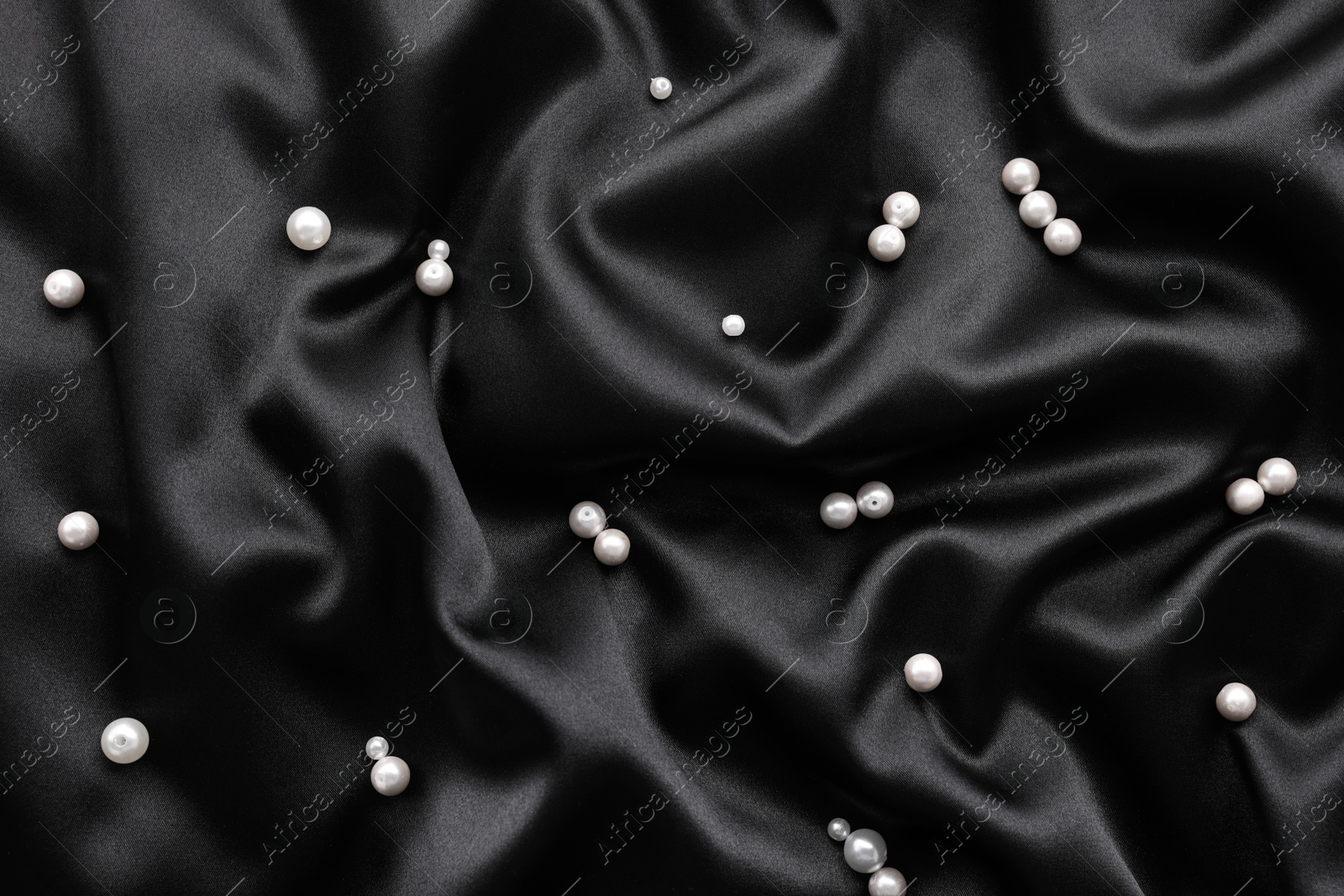 Photo of Many shiny pearls on black cloth, top view