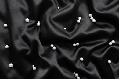 Photo of Many shiny pearls on black cloth, top view