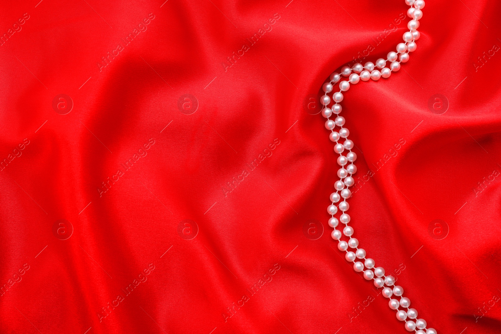 Photo of Beautiful pearl necklace on red cloth, top view. Space for text