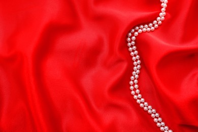 Photo of Beautiful pearl necklace on red cloth, top view. Space for text