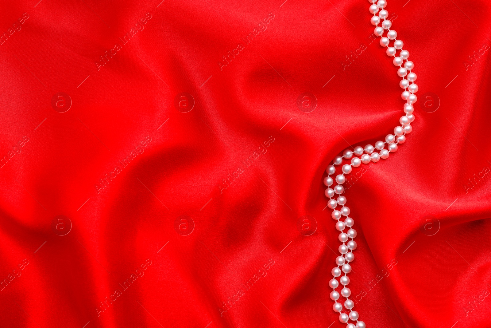 Photo of Beautiful pearl necklace on red cloth, top view. Space for text