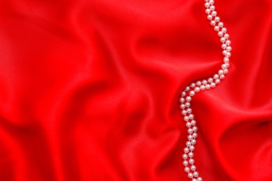 Photo of Beautiful pearl necklace on red cloth, top view. Space for text