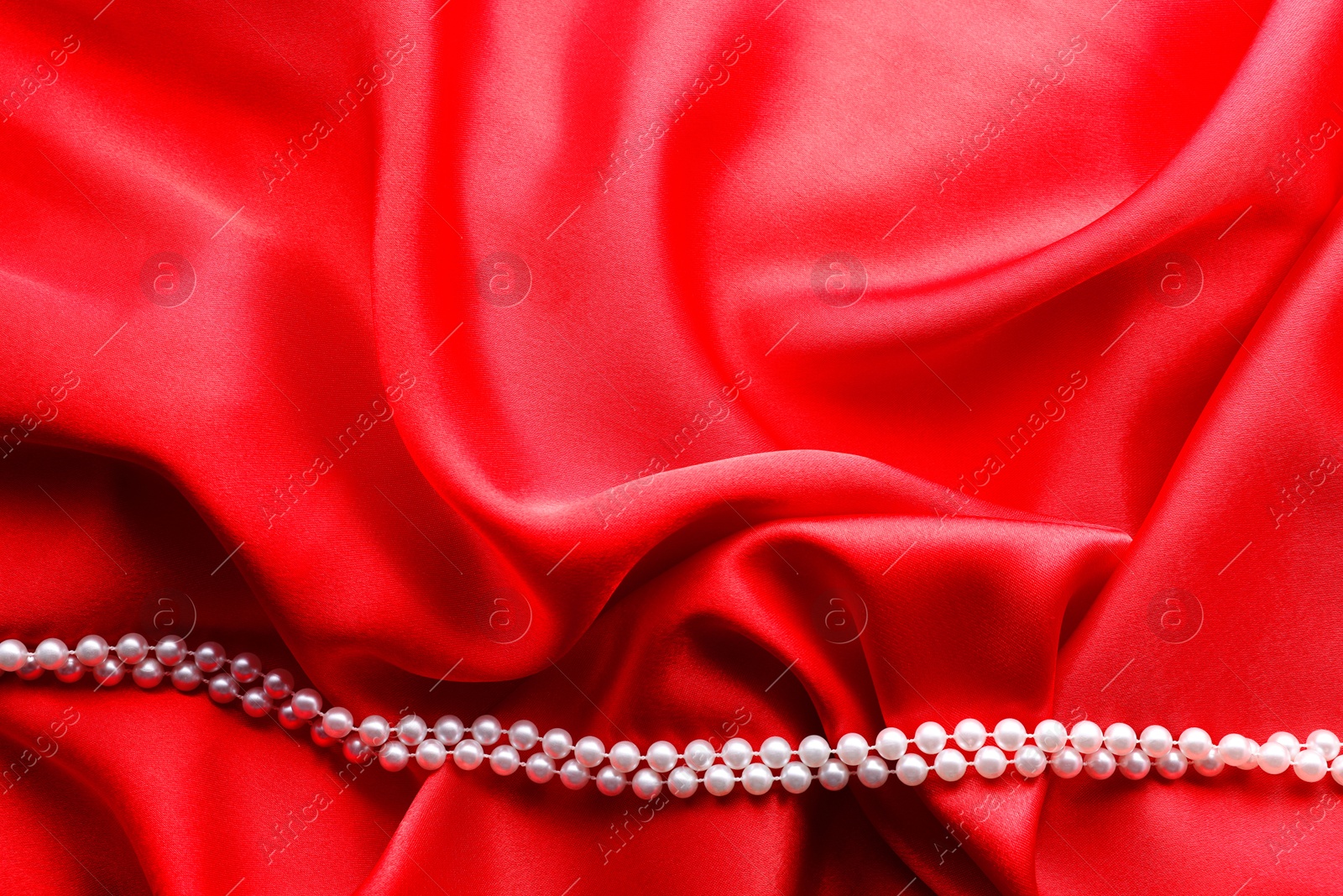 Photo of Beautiful pearl necklace on red cloth, top view. Space for text