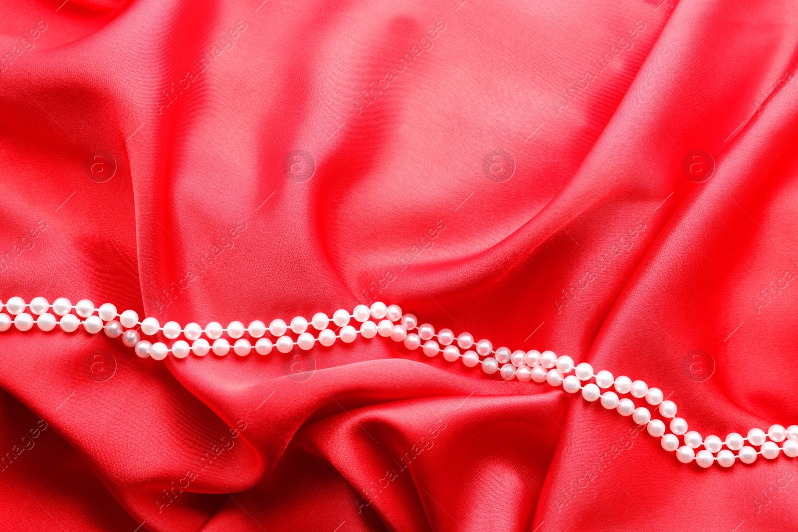 Photo of Beautiful pearl necklace on red cloth, top view. Space for text