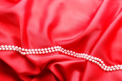 Photo of Beautiful pearl necklace on red cloth, top view. Space for text