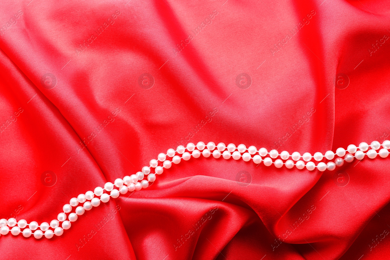 Photo of Beautiful pearl necklace on red cloth, top view. Space for text