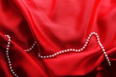 Photo of Beautiful pearl necklace on red cloth, top view