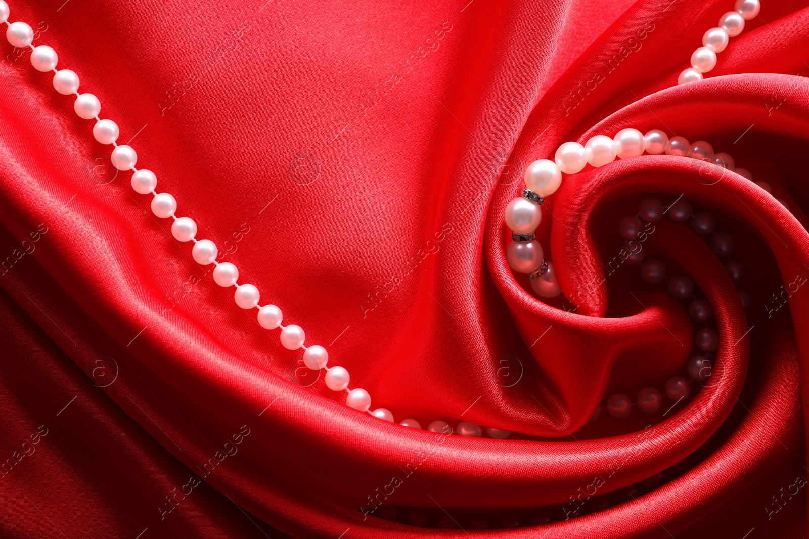 Photo of Beautiful pearl necklace on red cloth, top view