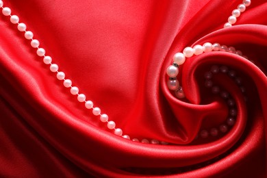 Photo of Beautiful pearl necklace on red cloth, top view