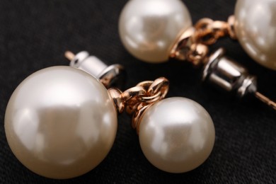 Photo of Beautiful pearl earrings on black cloth, macro view