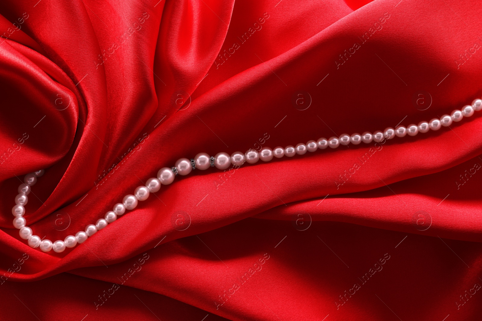 Photo of Beautiful pearl necklace on red cloth, top view