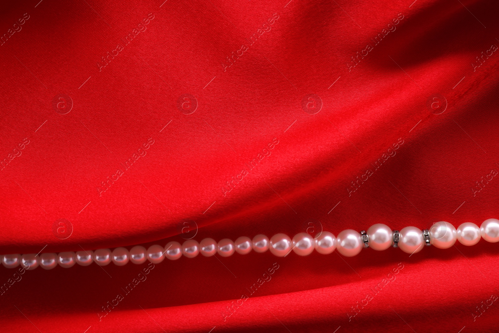 Photo of Beautiful pearl necklace on red cloth, top view. Space for text