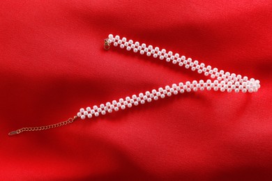 Photo of Beautiful pearl necklace on red cloth, top view