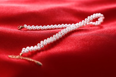 Photo of Beautiful pearl necklace on red cloth, closeup