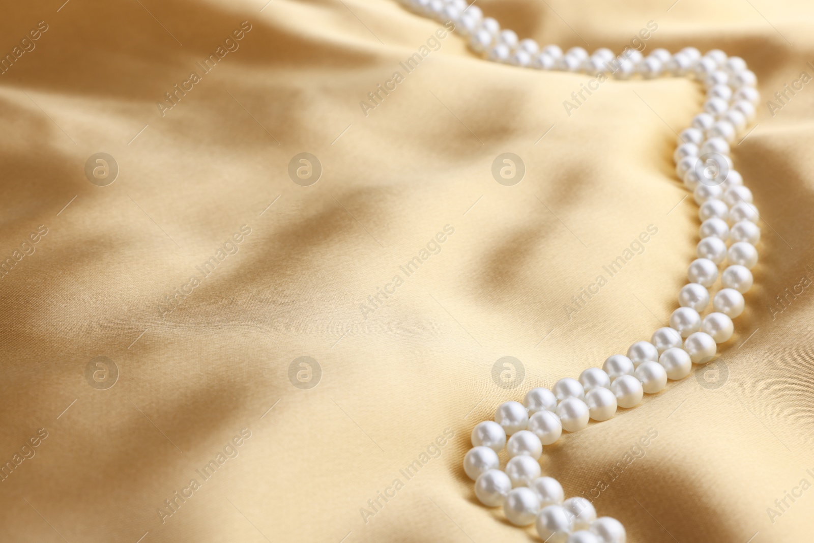 Photo of Beautiful pearl necklace on golden silk, closeup. Space for text