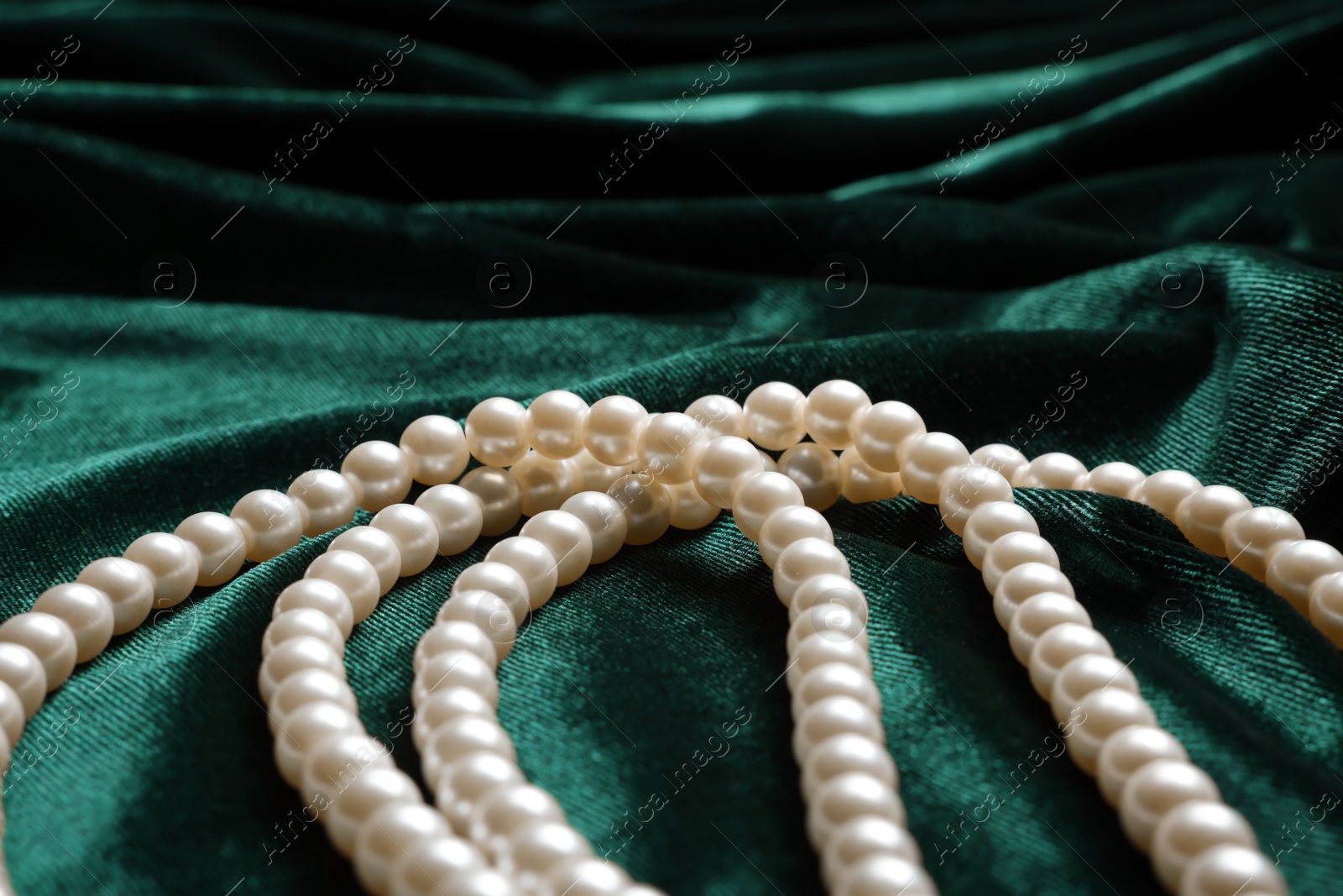 Photo of Beautiful pearl necklace on green cloth, closeup