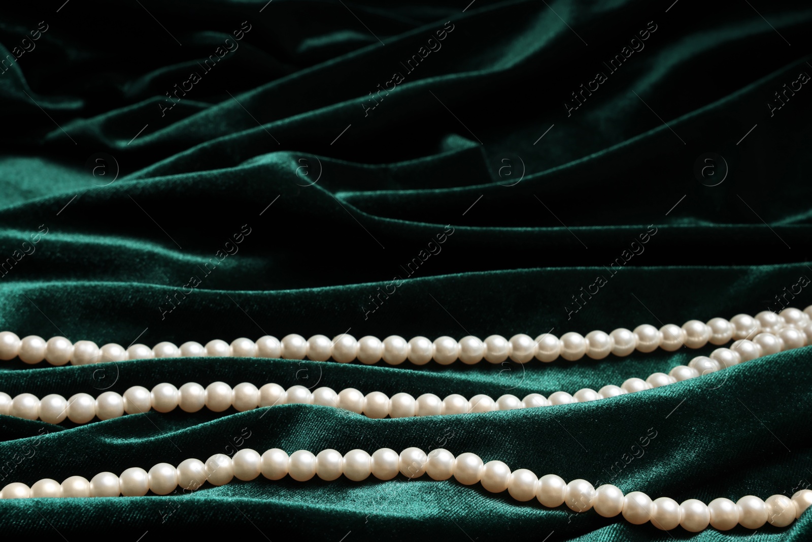 Photo of Beautiful pearl necklace on green cloth, closeup. Space for text