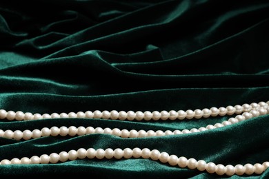 Photo of Beautiful pearl necklace on green cloth, closeup. Space for text