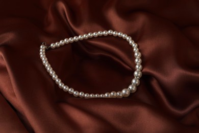 Photo of Beautiful pearl necklace on brown silky fabric