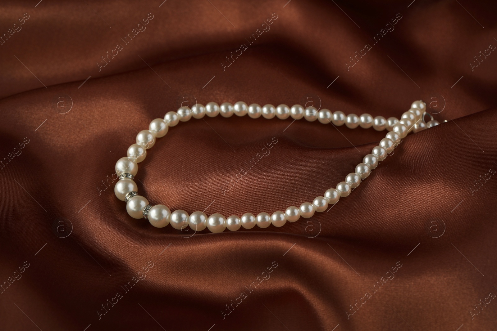 Photo of Beautiful pearl necklace on brown silky fabric