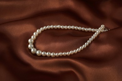 Photo of Beautiful pearl necklace on brown silky fabric