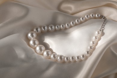 Photo of Beautiful pearl necklace on white silk, closeup