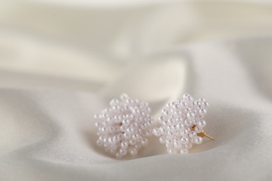 Photo of Beautiful pearl earrings on white silk, closeup