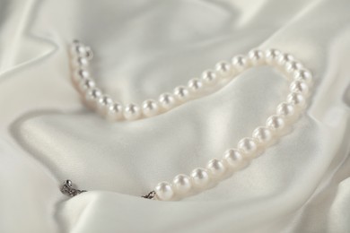 Photo of Beautiful pearl necklace on white silk, closeup