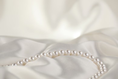 Photo of Beautiful pearl necklace on white silk, closeup