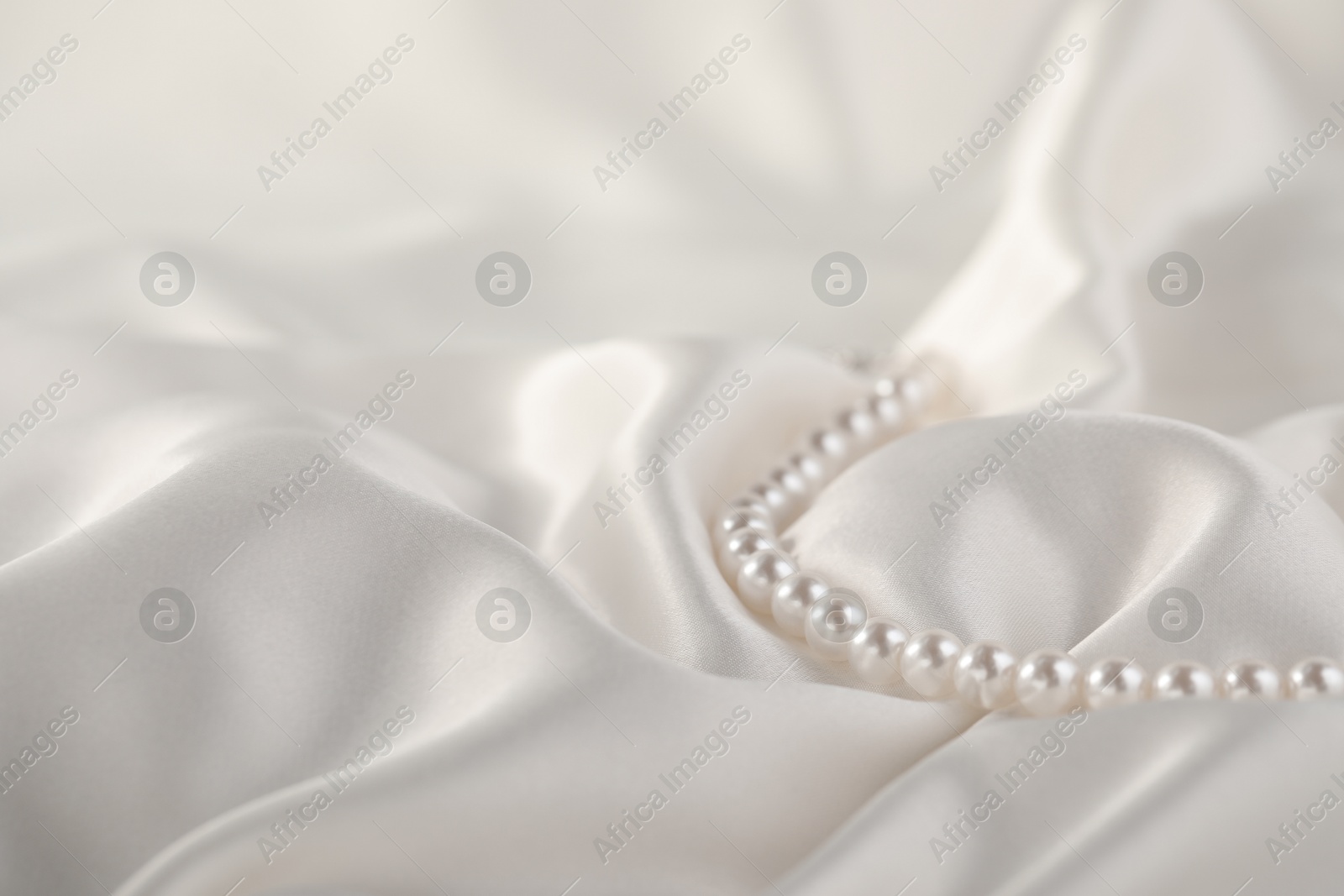 Photo of Beautiful pearl necklace on white silk, closeup. Space for text