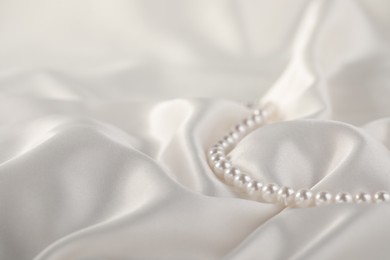 Photo of Beautiful pearl necklace on white silk, closeup. Space for text