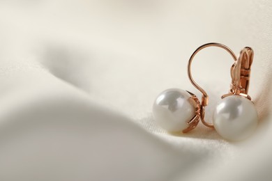 Photo of Beautiful pearl earrings on white silk, closeup. Space for text