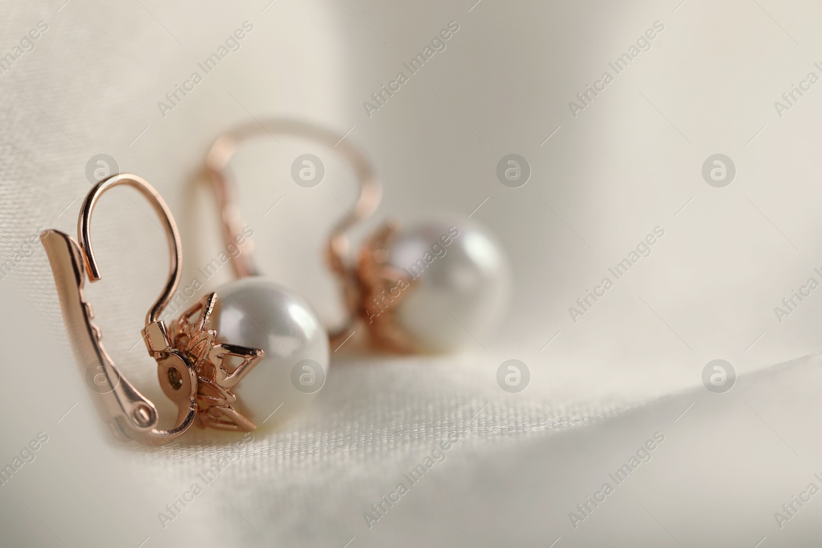 Photo of Beautiful pearl earrings on white silk, closeup. Space for text