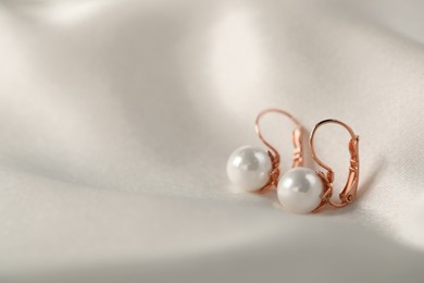 Photo of Beautiful pearl earrings on white silk, closeup. Space for text