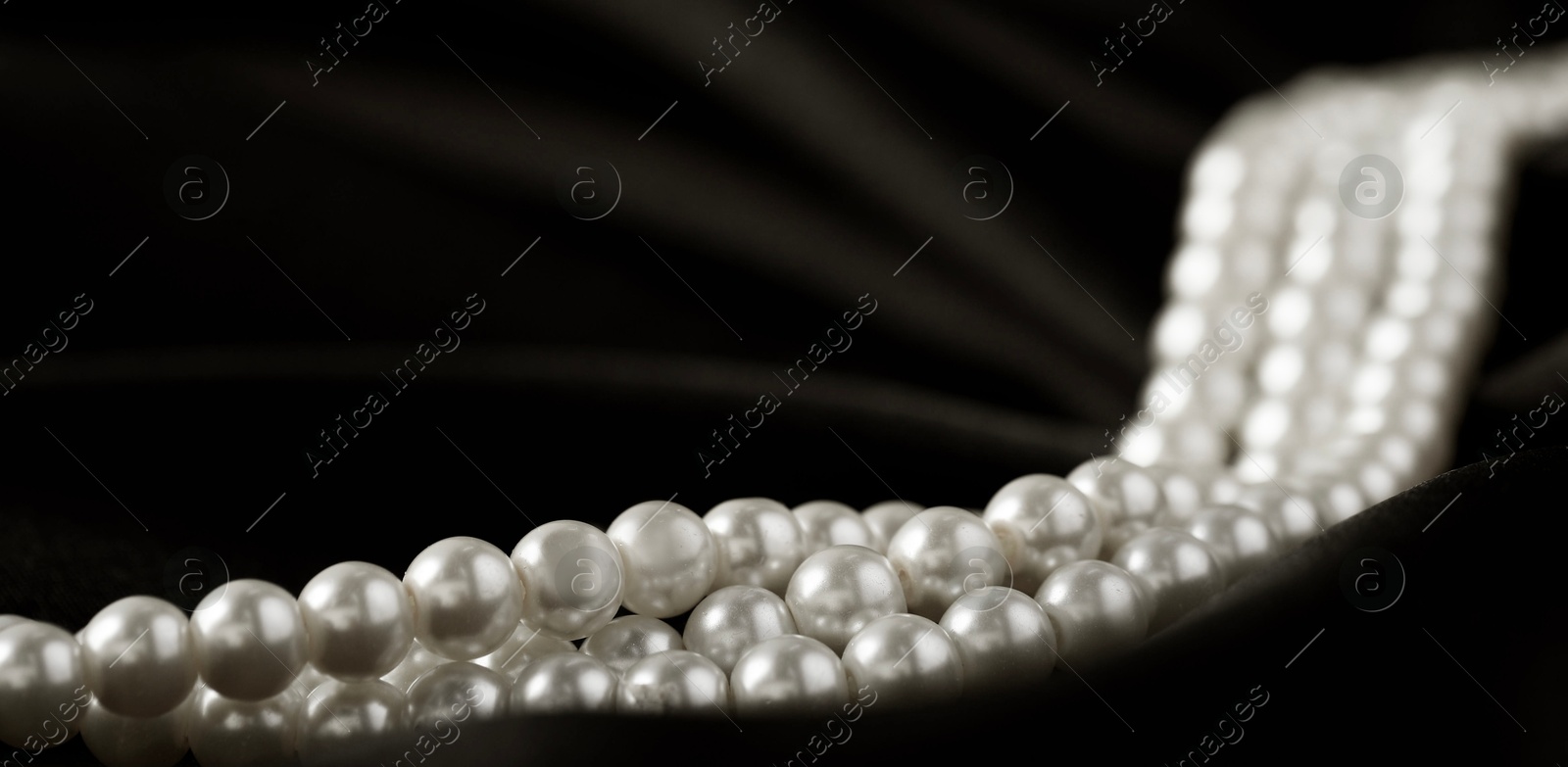 Photo of Beautiful pearl necklace on black silk, closeup. Space for text