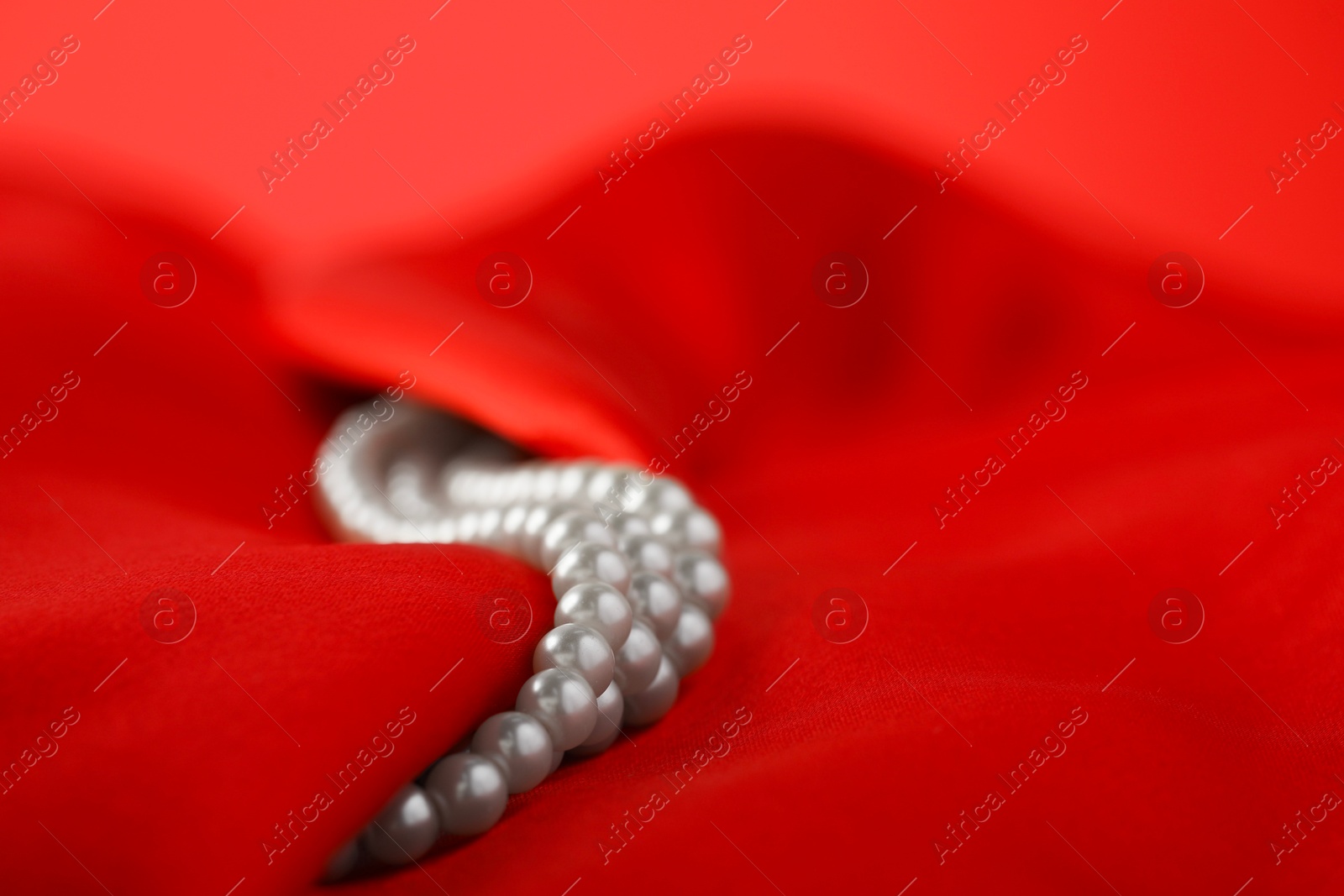 Photo of Beautiful pearl necklace on red silk, closeup. Space for text