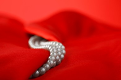 Photo of Beautiful pearl necklace on red silk, closeup. Space for text