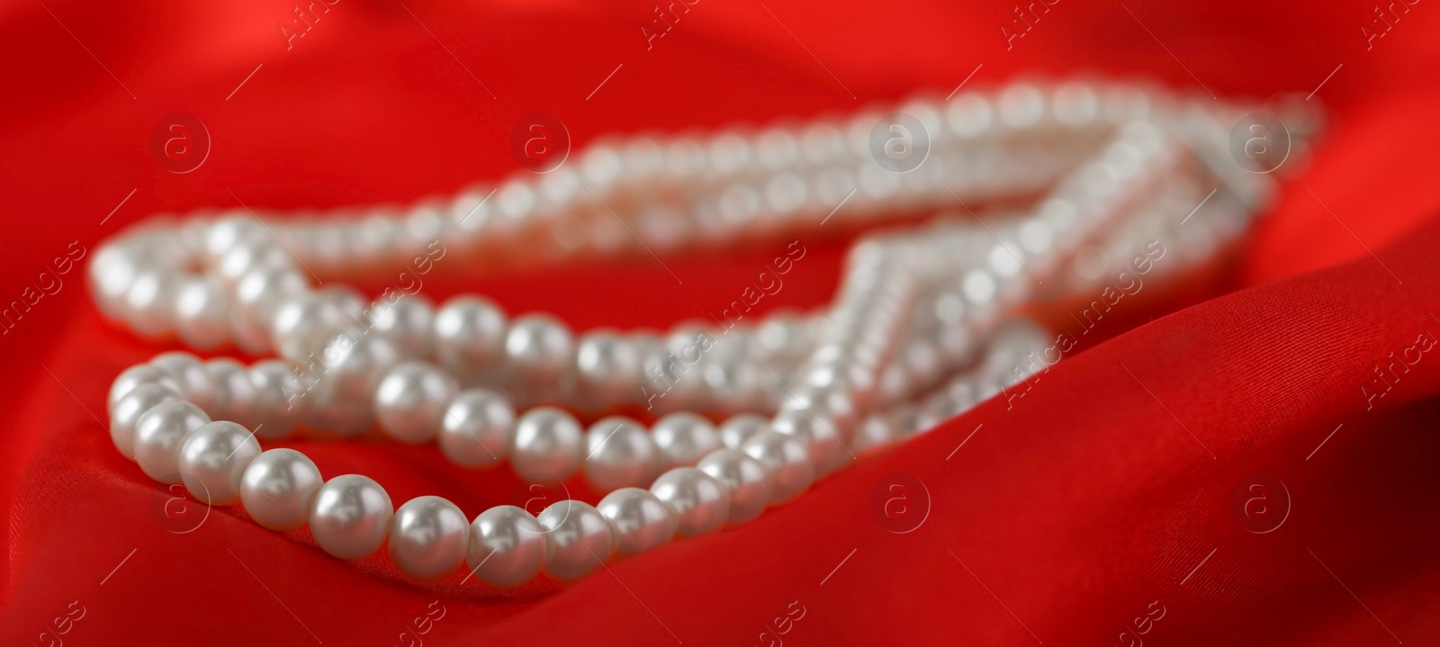 Photo of Beautiful pearl necklace on red silk, closeup