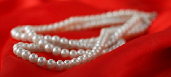 Photo of Beautiful pearl necklace on red silk, closeup