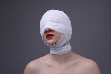 Photo of Woman with face wrapped in medical bandage after plastic surgery operation on grey background