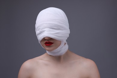 Photo of Woman with face wrapped in medical bandage after plastic surgery operation on grey background