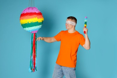 Photo of Man with tied eyes breaking pinata on light blue background