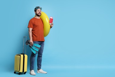 Photo of Traveller with passport, ticket, suitcase and beach accessories on light blue background, space for text