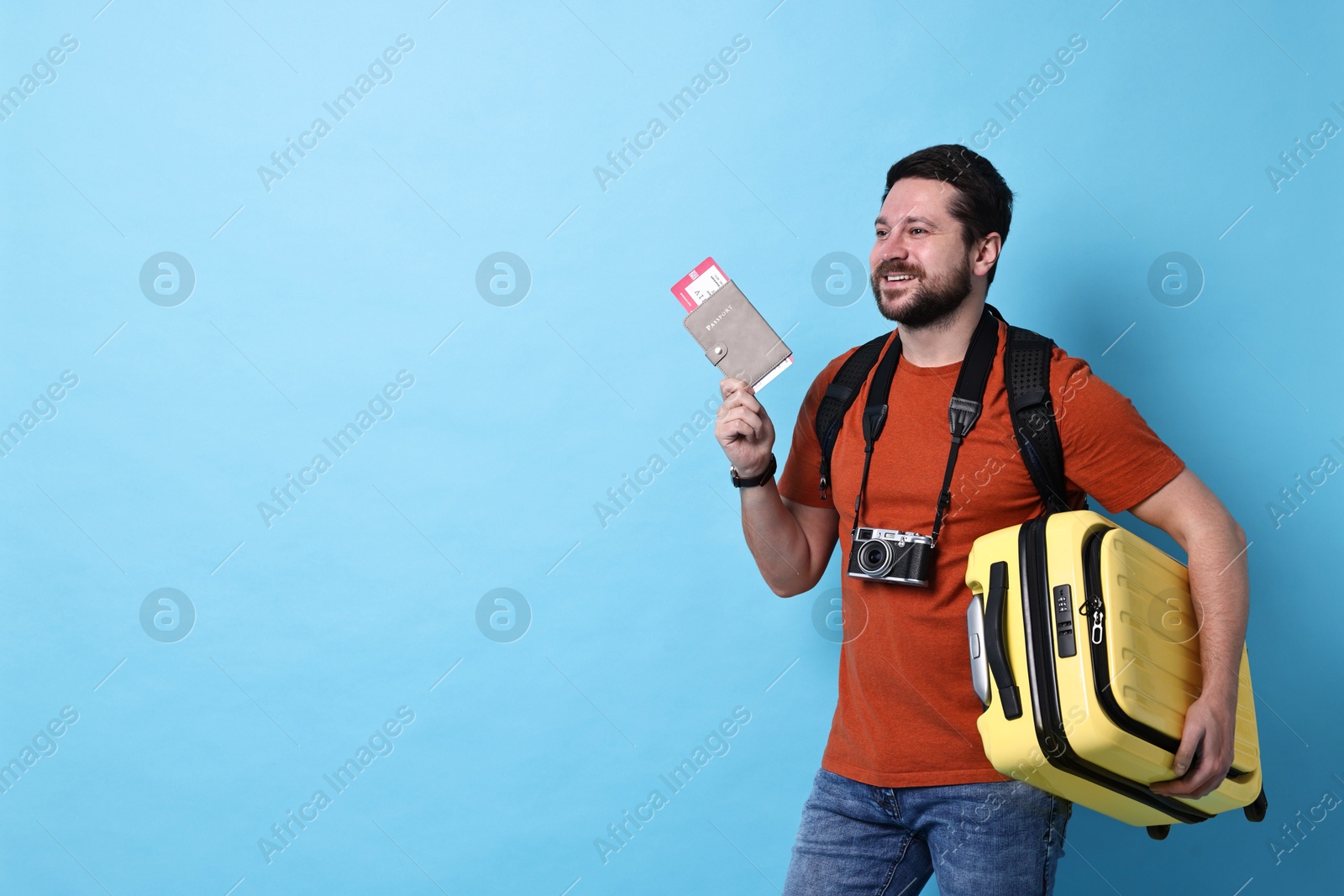 Photo of Traveller with passport, ticket and suitcase on light blue background, space for text