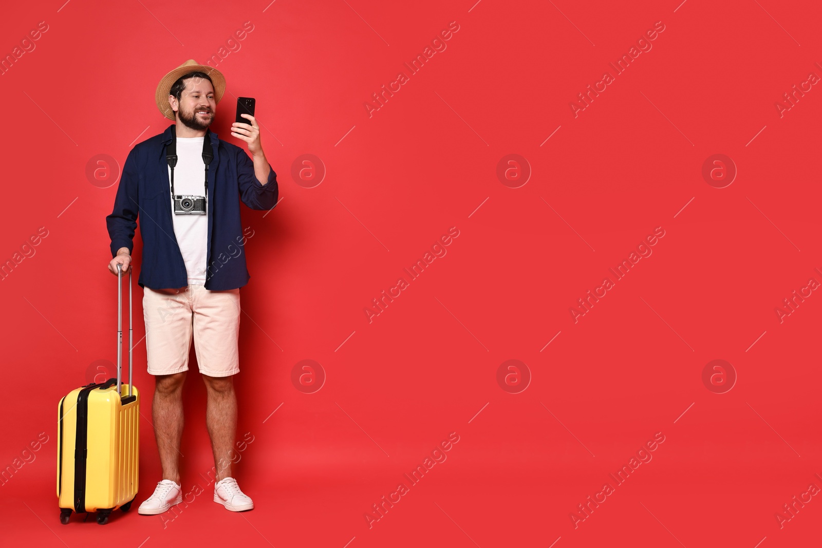 Photo of Traveller with suitcase using smartphone on red background, space for text